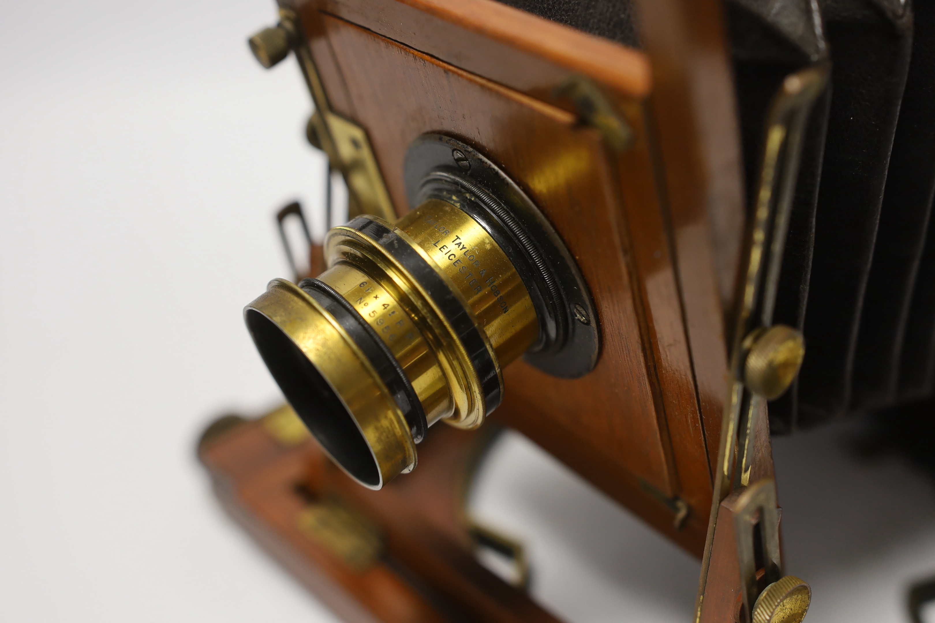 A late nineteenth century brass and mahogany half plate bellows camera with a lens and a shutter action by Taylor, Taylor & Hobson, Leicester, together with a negative holder